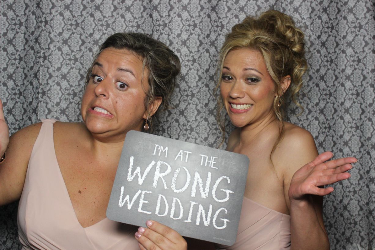 Two women in a photo booth holding up a sign.